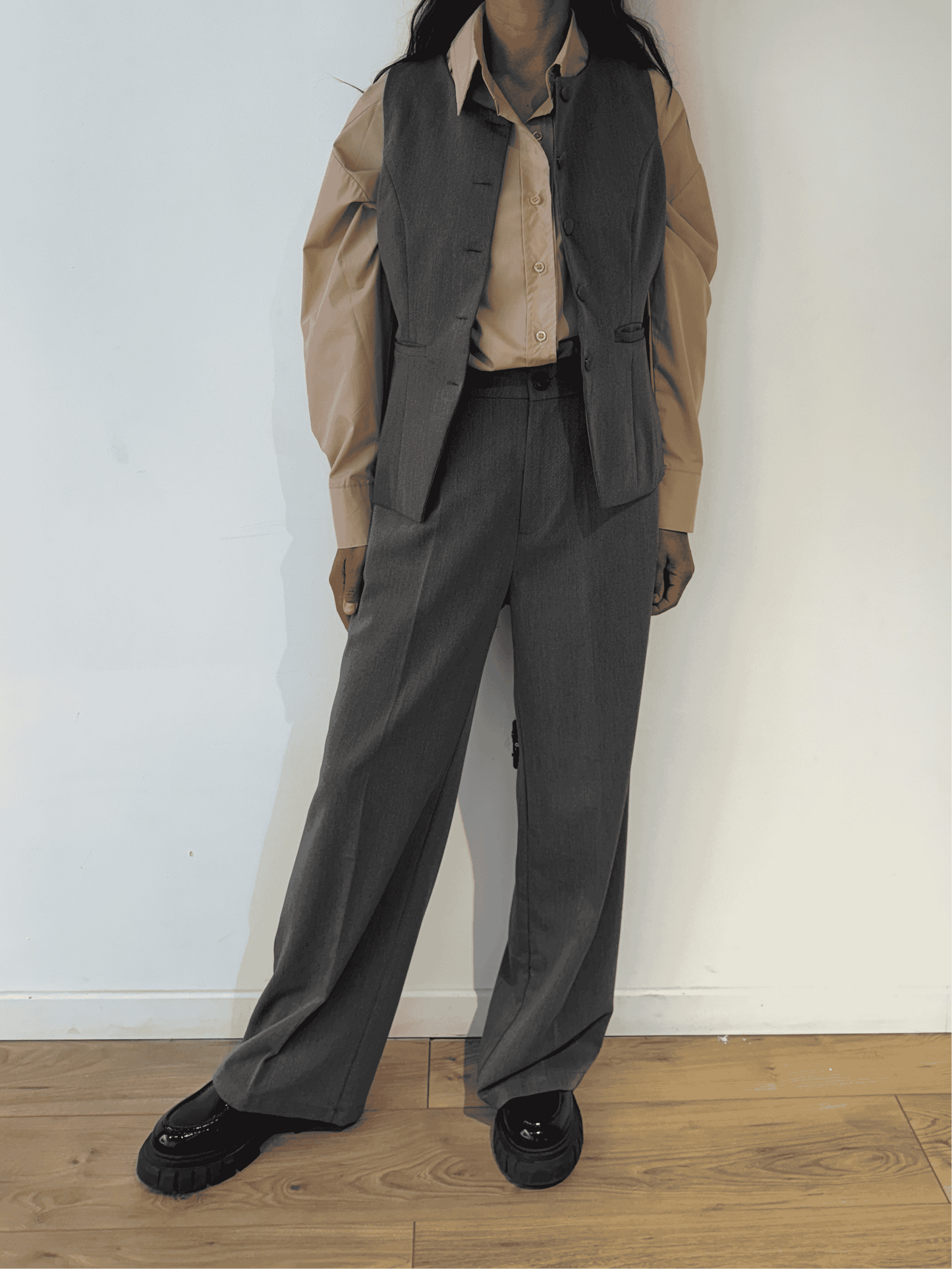 Femme portant un blazer sans manches gris avec une chemise beige, vue de face.