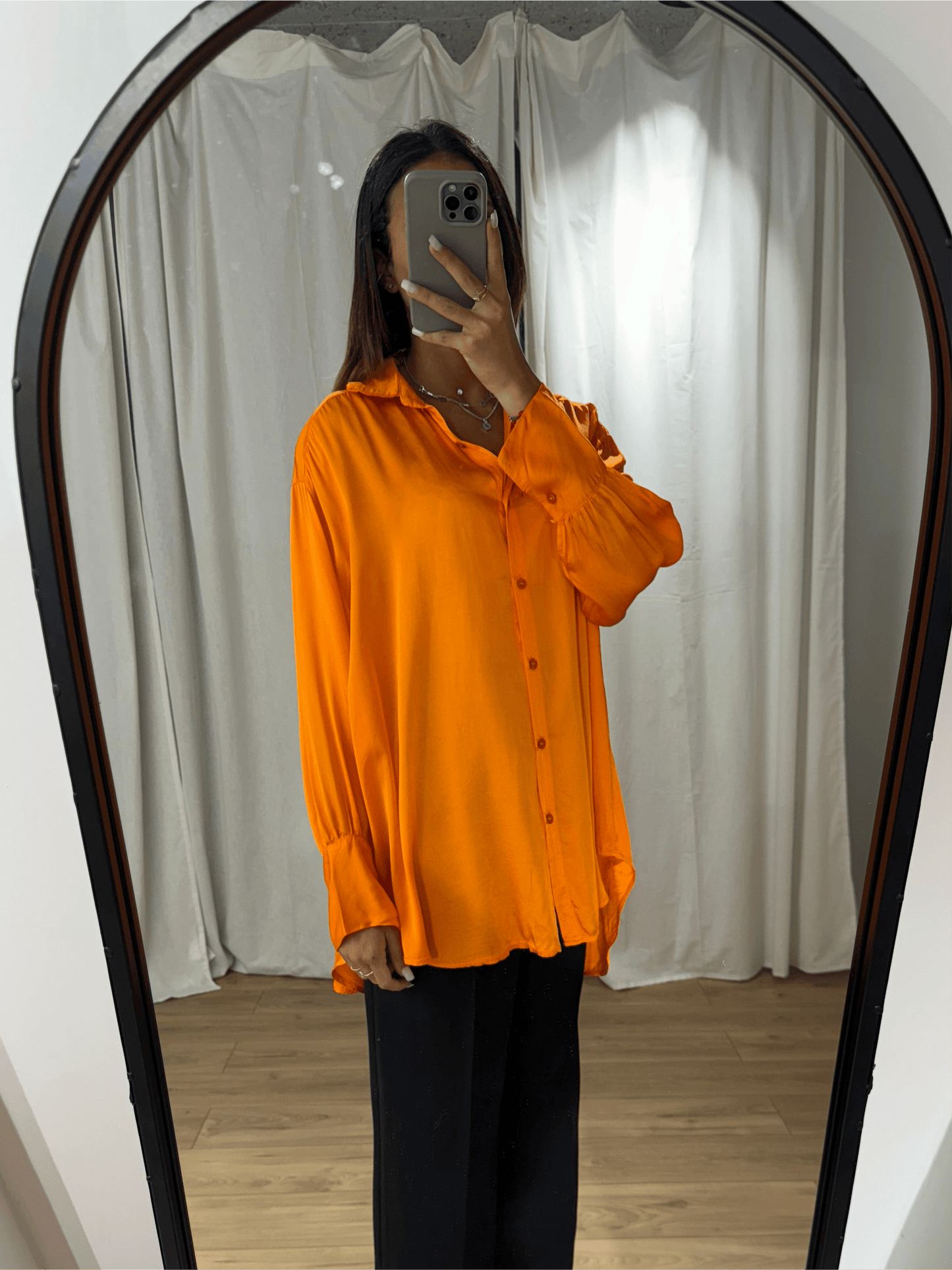 Femme portant une chemise en soie orange vibrante, vue de face devant un miroir.