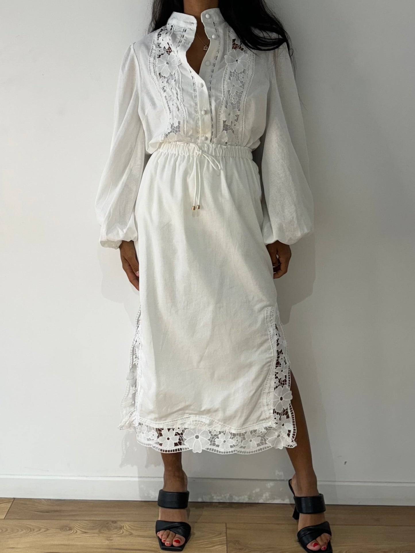 Vue complète de face de l'ensemble chemise et jupe en dentelle blanche porté avec des talons noirs.