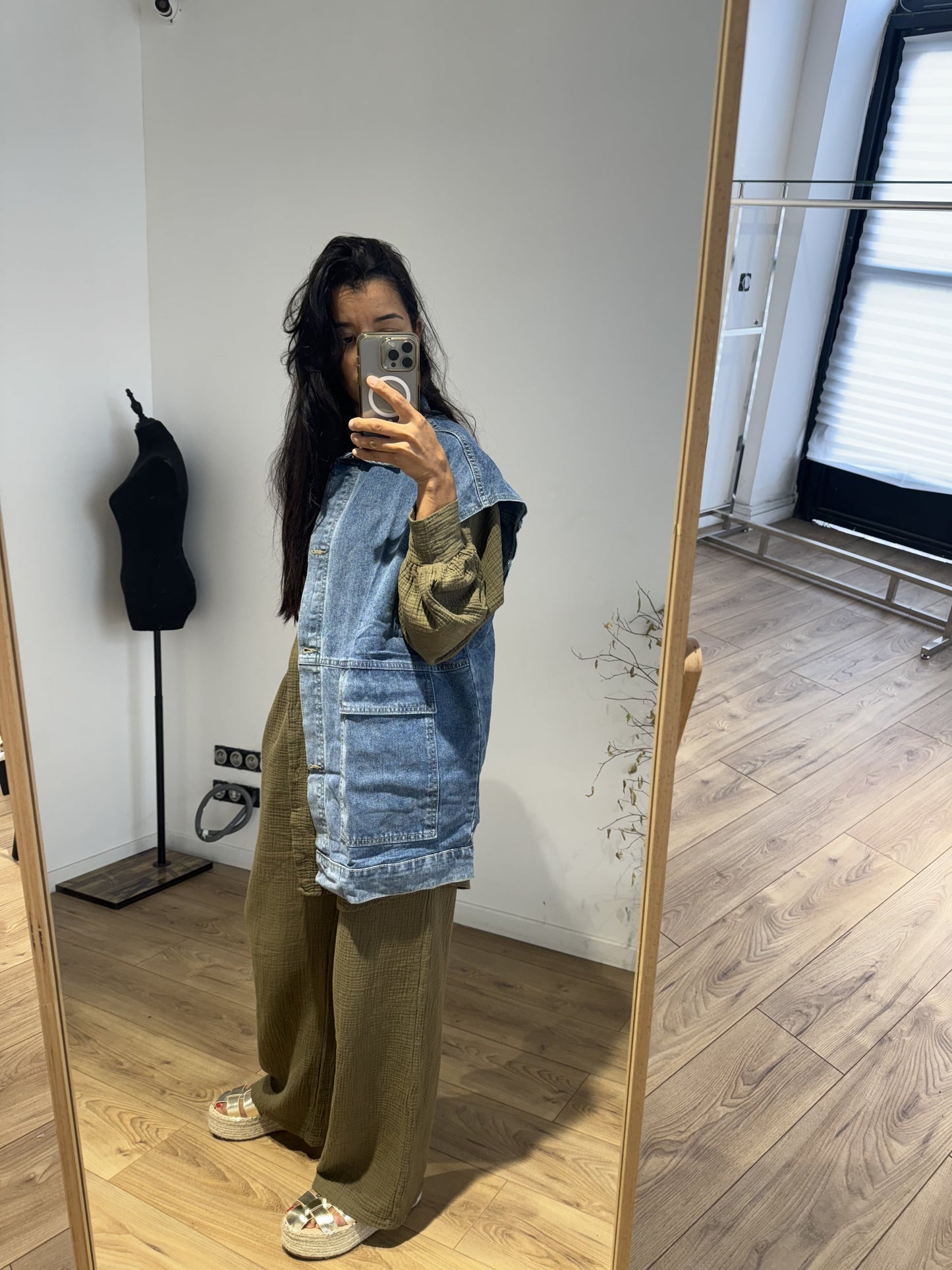 Femme portant un ensemble chemise et pantalon en gaze de coton vert kaki, avec une veste en jean par-dessus, prise en selfie devant un miroir.