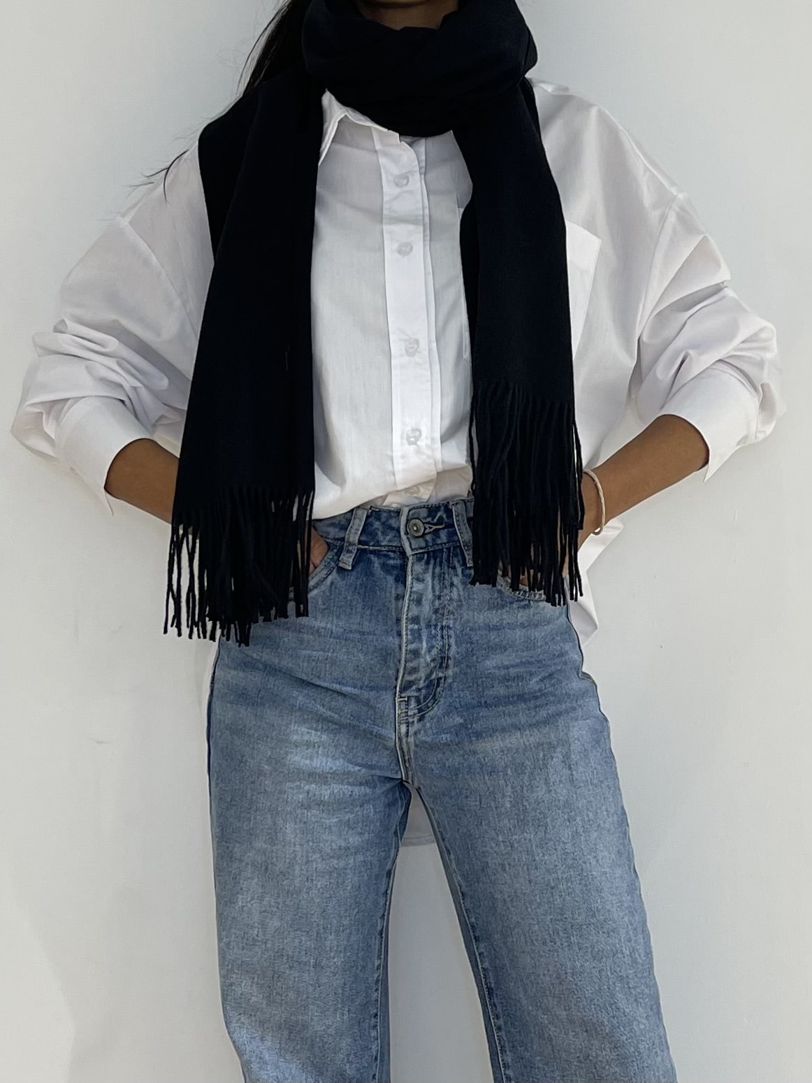 Étole noire élégante avec des franges, portée comme un accessoire chic sur une chemise blanche, créant un contraste saisissant.