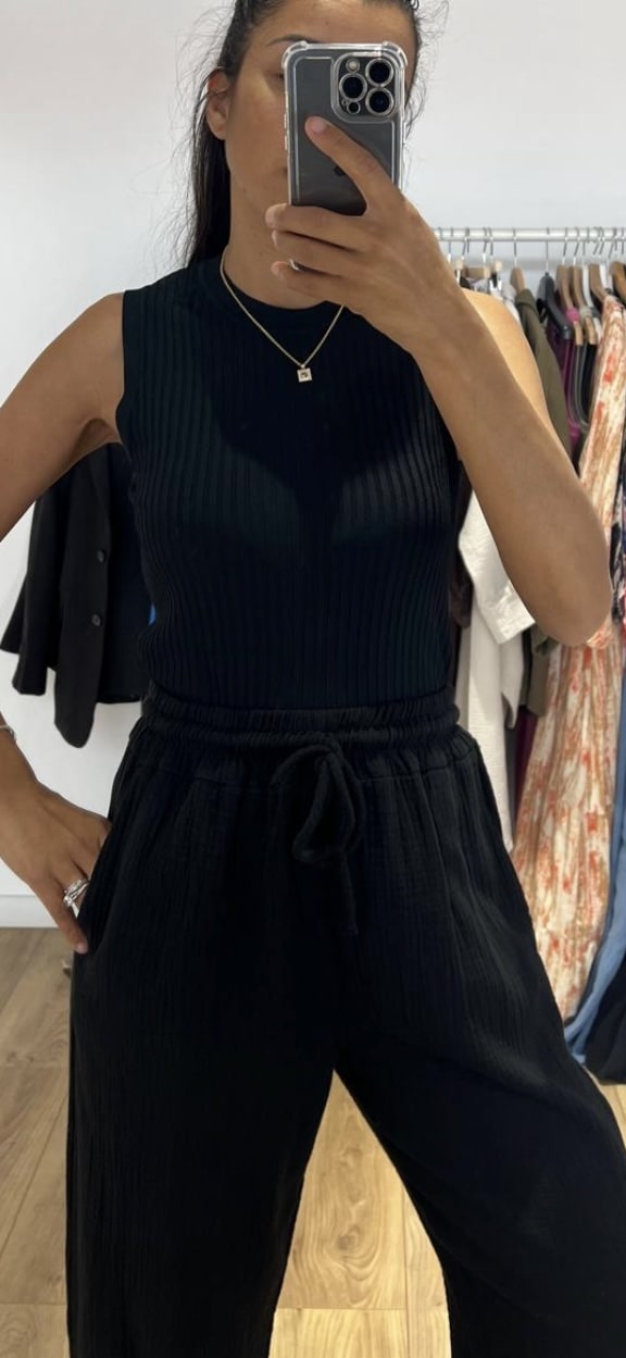 Gros plan sur une femme portant un haut sans manche noir, prenant un selfie devant un miroir.