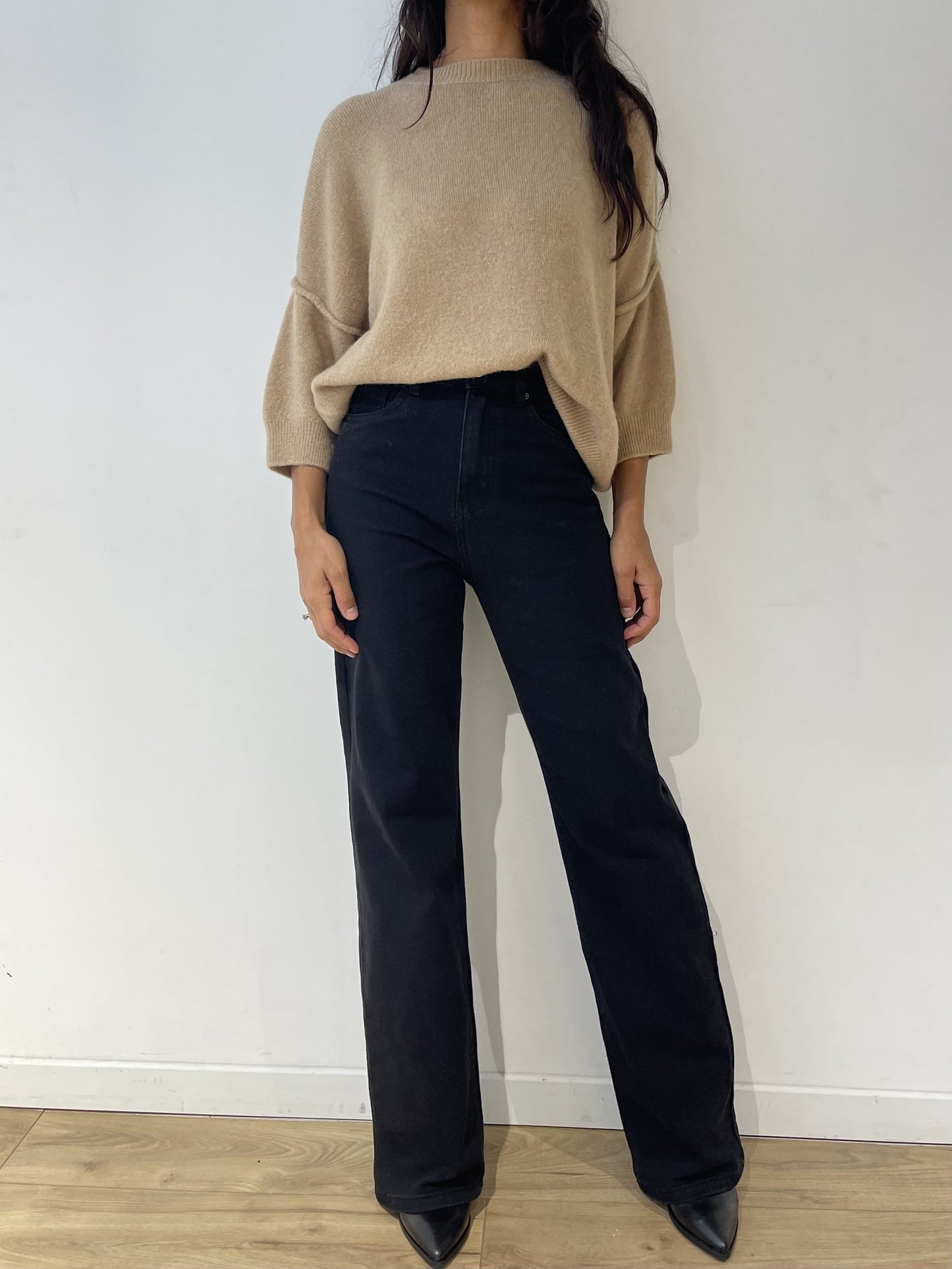 Jean coupe droite noir pour femme, porté avec un pull beige oversize et des bottines noires.