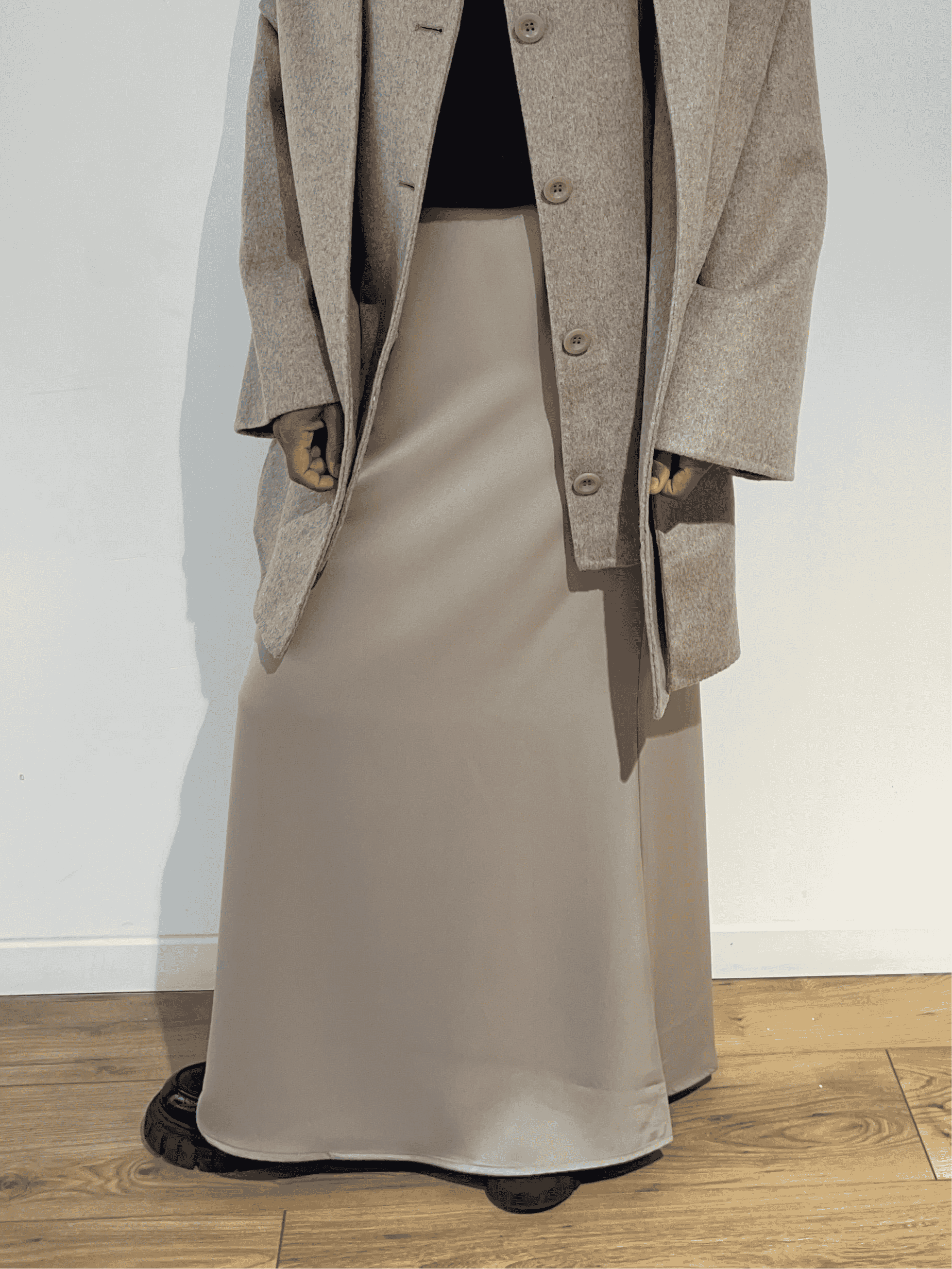 Femme portant une jupe longue en satin beige, vue de face avec manteau long