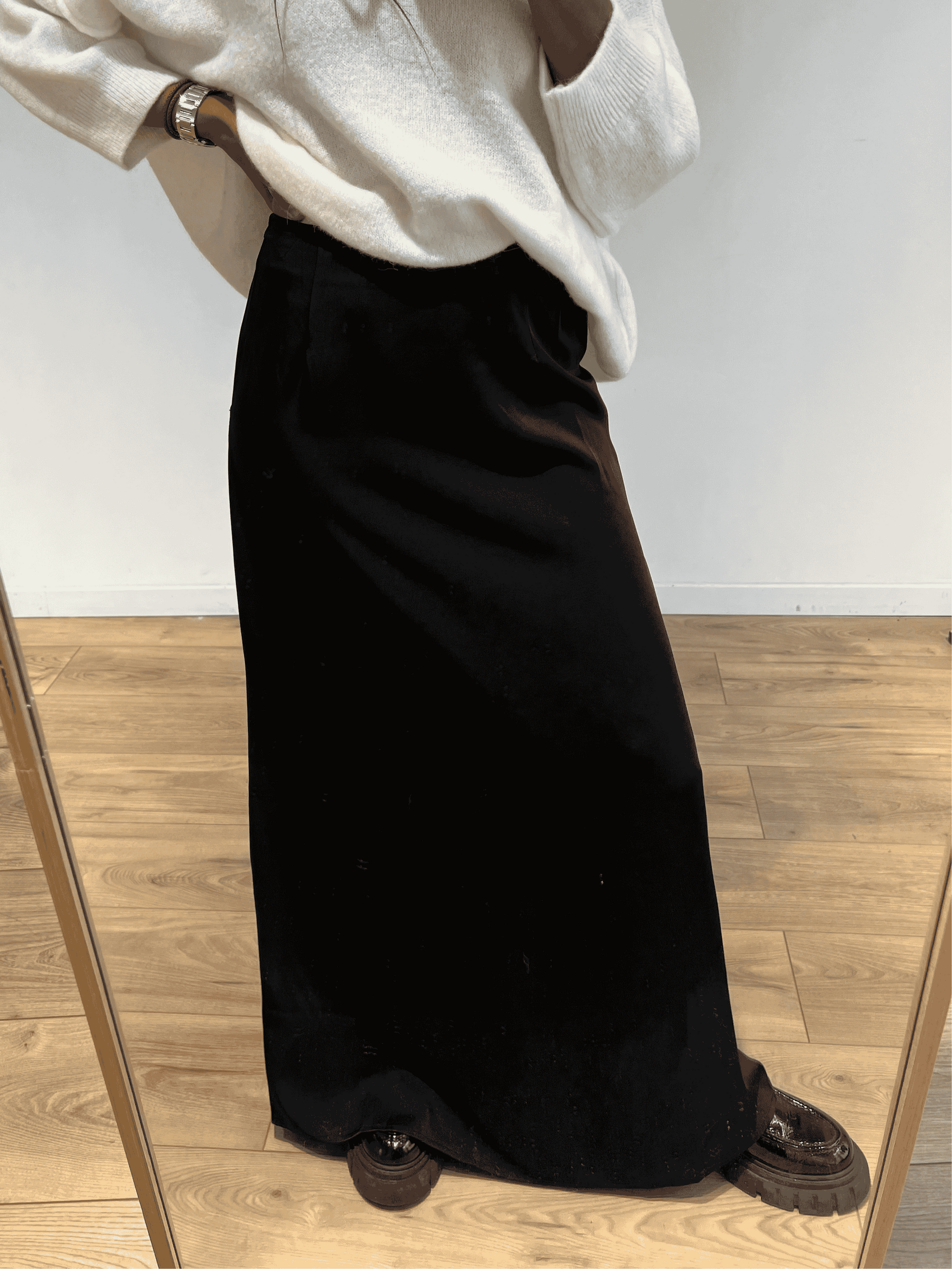 Femme portant une jupe longue en satin noir, vue de face avec pull blanc