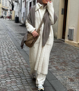 Femme en tenue hivernale avec manteau long écrue et hijab assorti dans un décor urbain