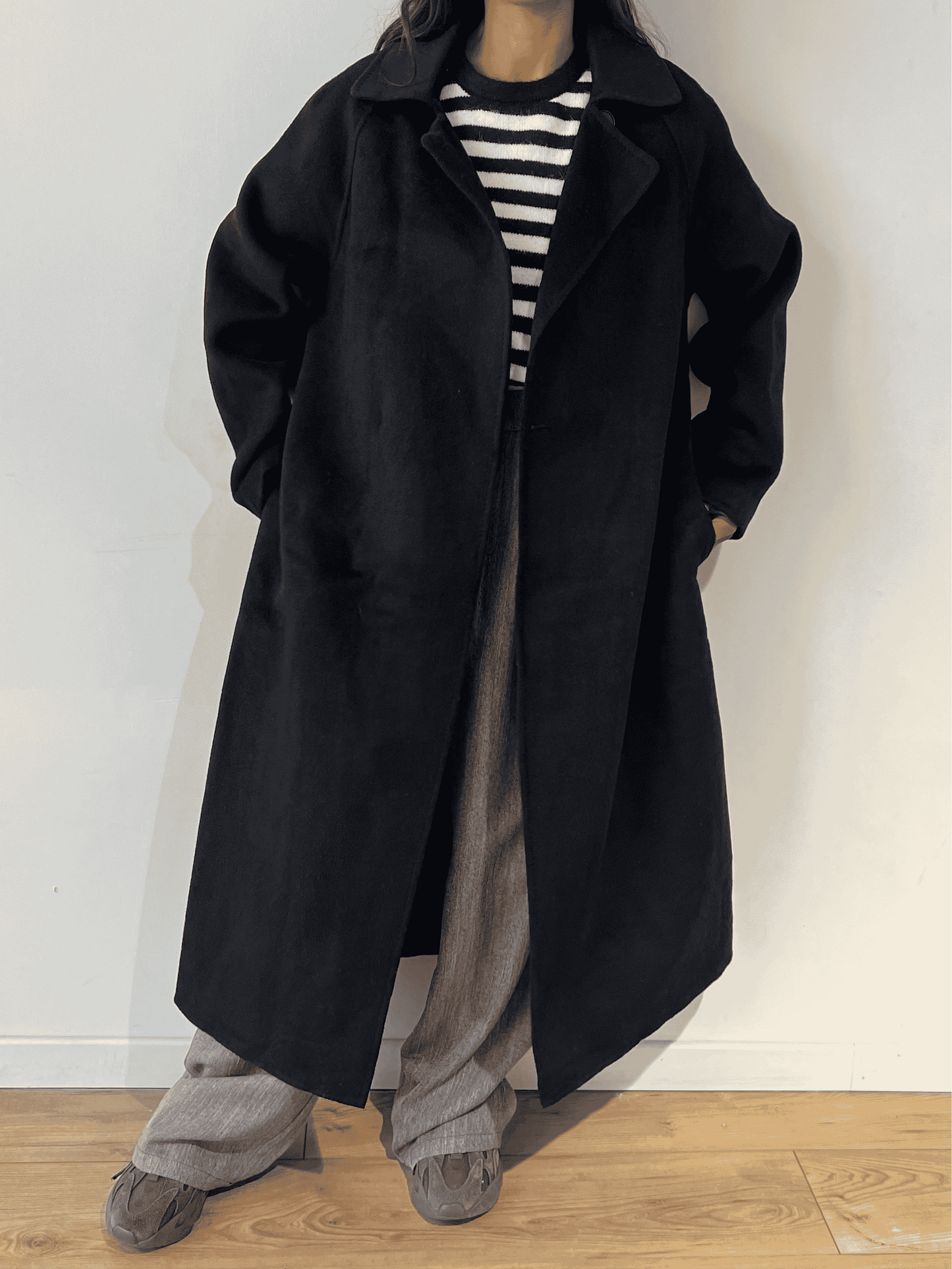 Long manteau noir porté sur un pull marinière et un pantalon gris.