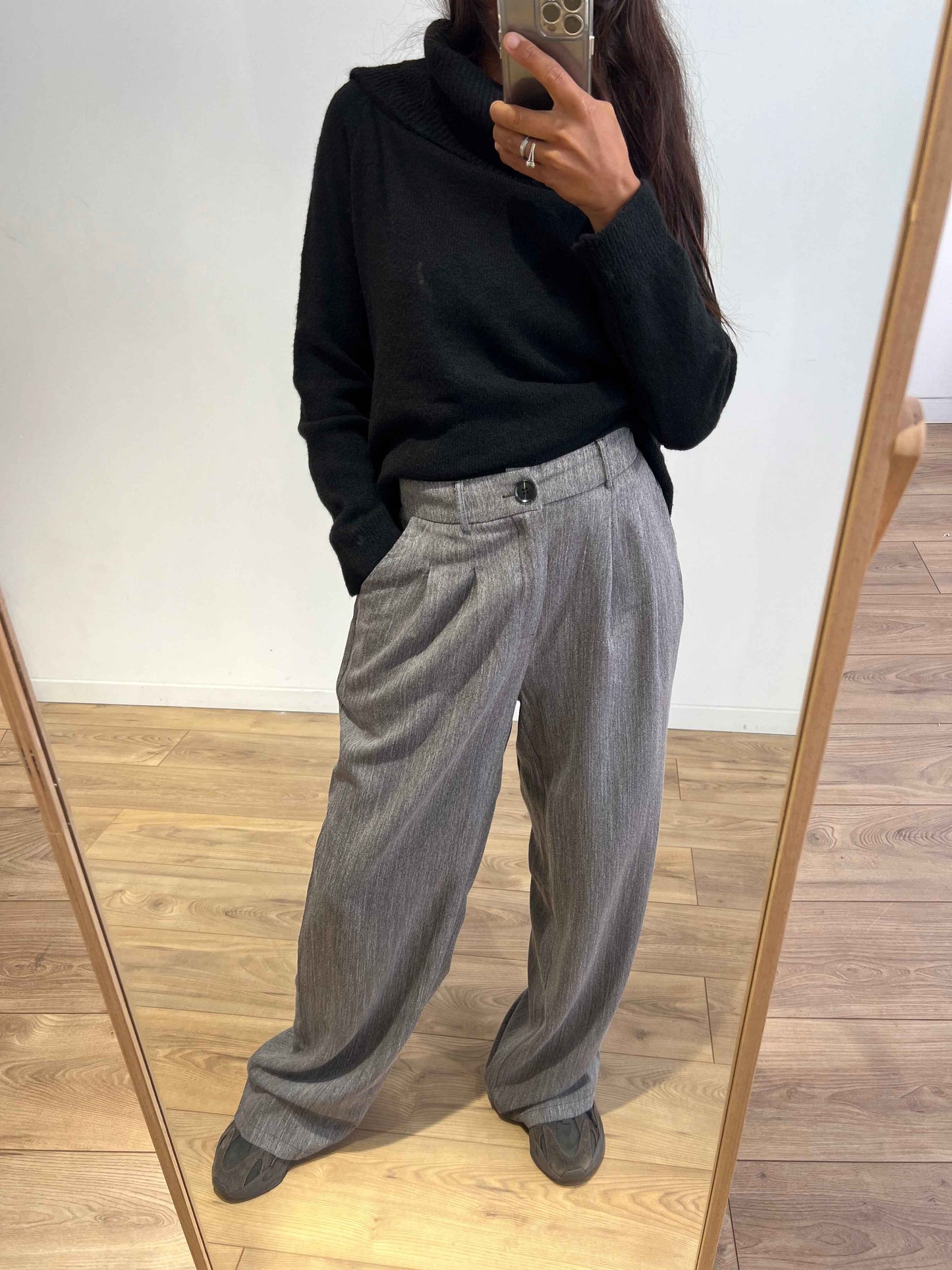 Femme portant un pantalon gris ample et un pull noir à col cheminée, prise de vue de face.