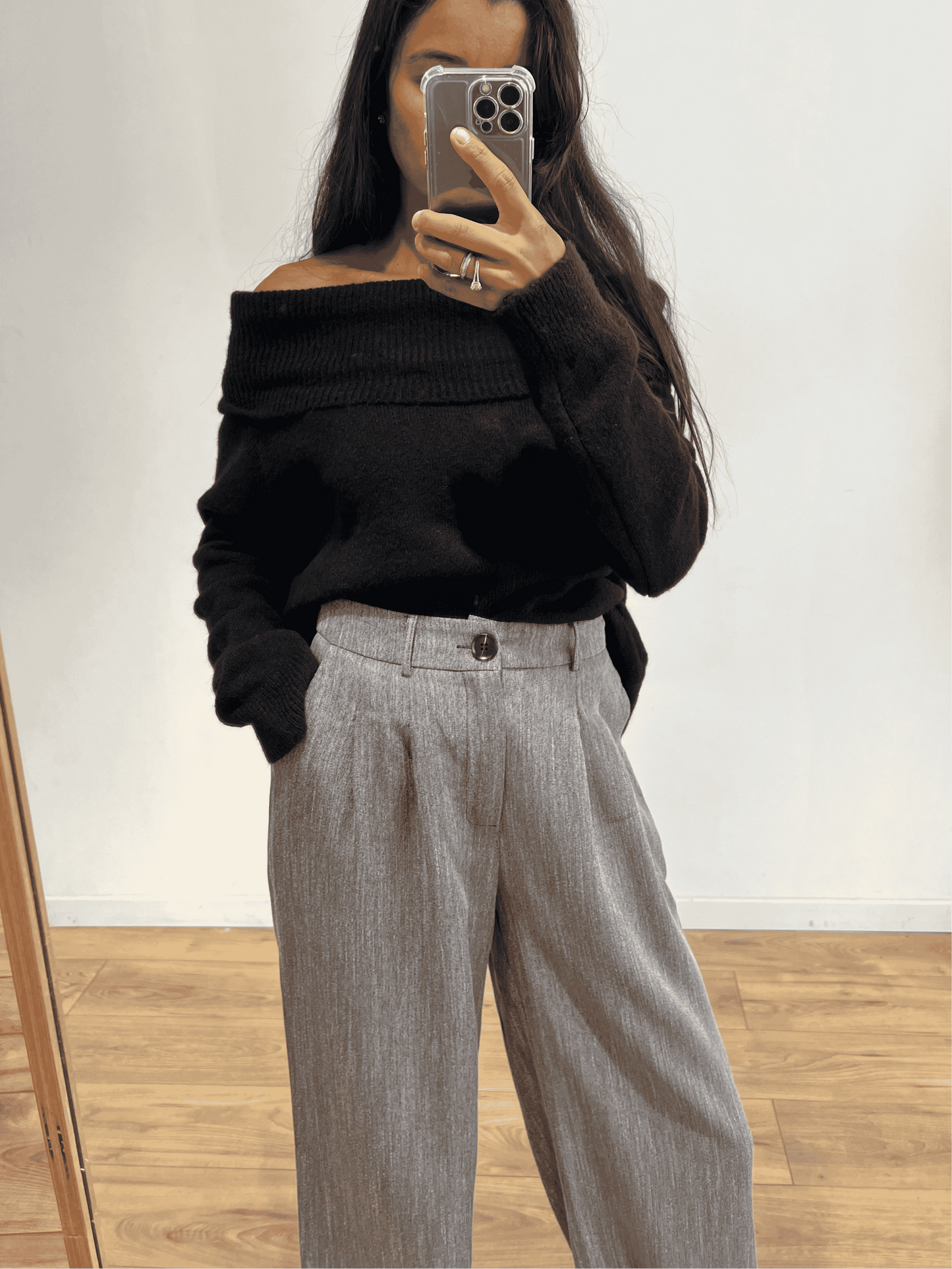 Femme portant un pantalon gris ample avec un pull noir col bateau, vue de face.