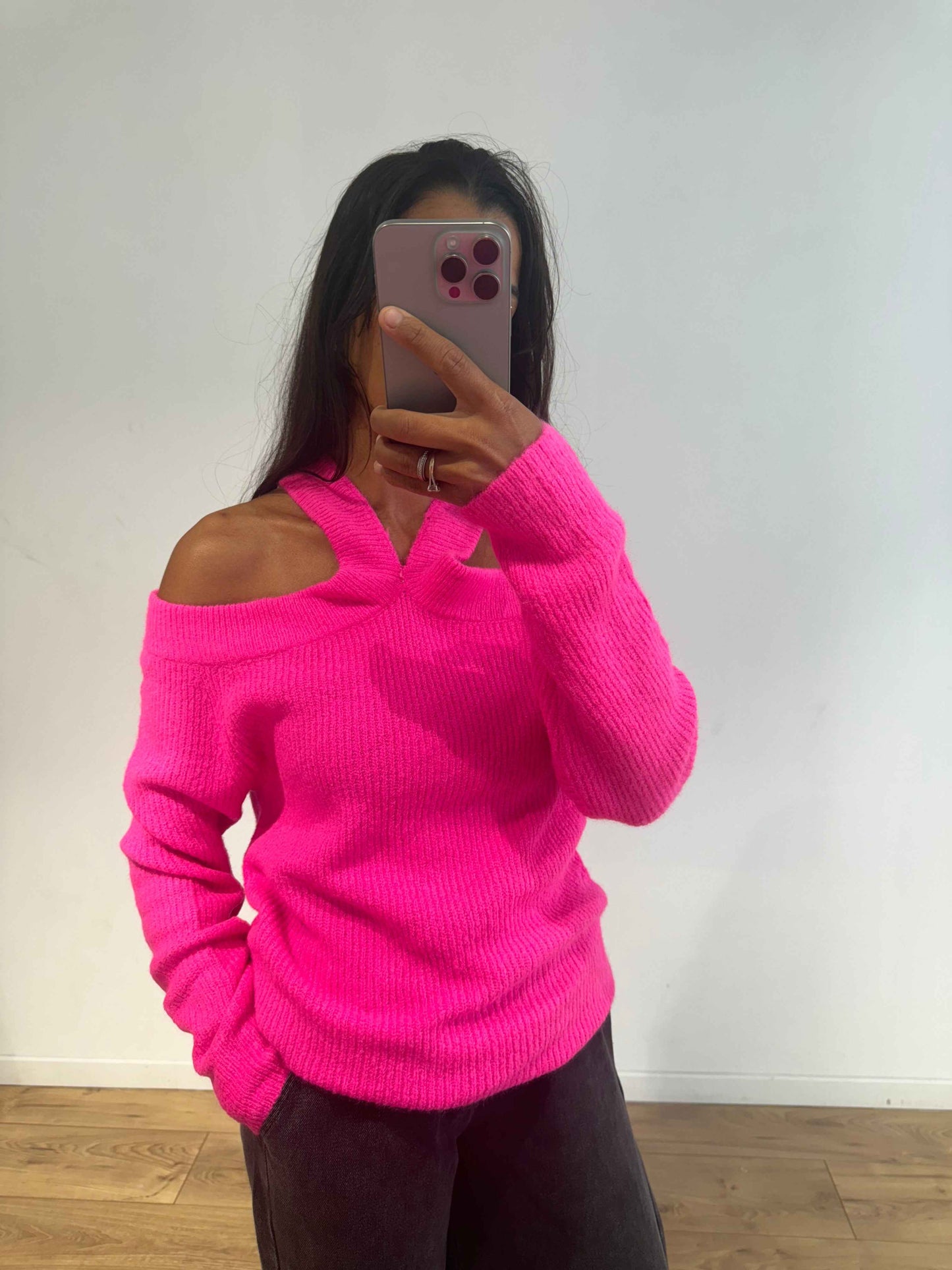 Femme portant un pull rose en maille avec épaules dénudées, vue de face.