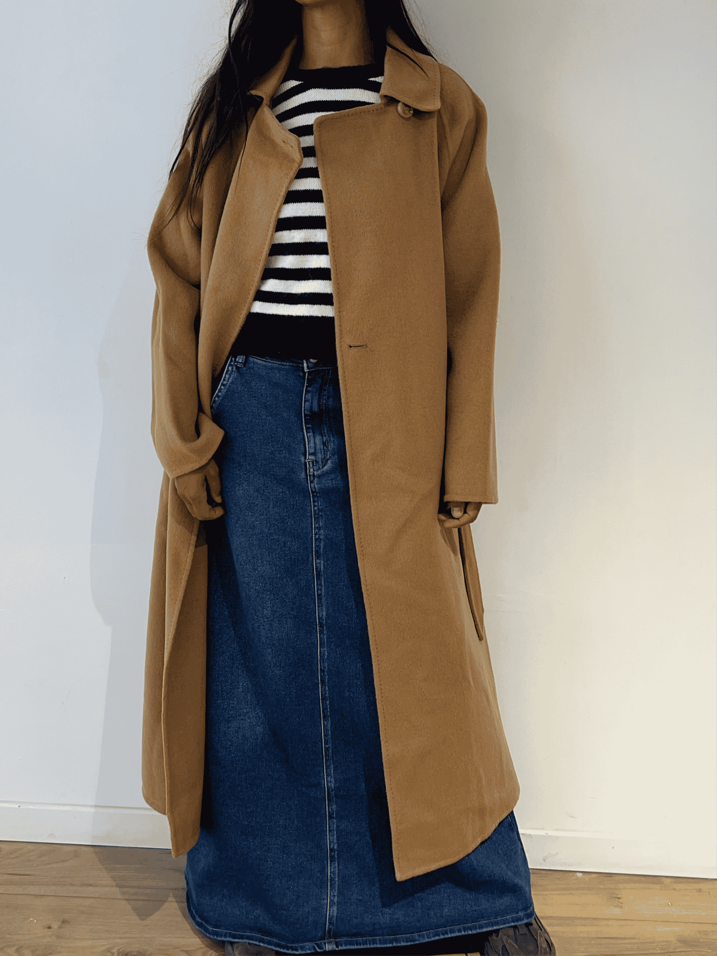 Femme portant un pull marinière noir et blanc avec un cœur rouge, un manteau camel et une jupe en denim, vue de face.