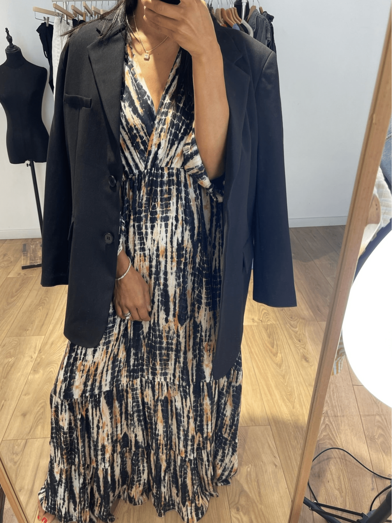 Femme portant une robe longue tie and dye en soie noire avec un blazer noir, prise en selfie devant un miroir.