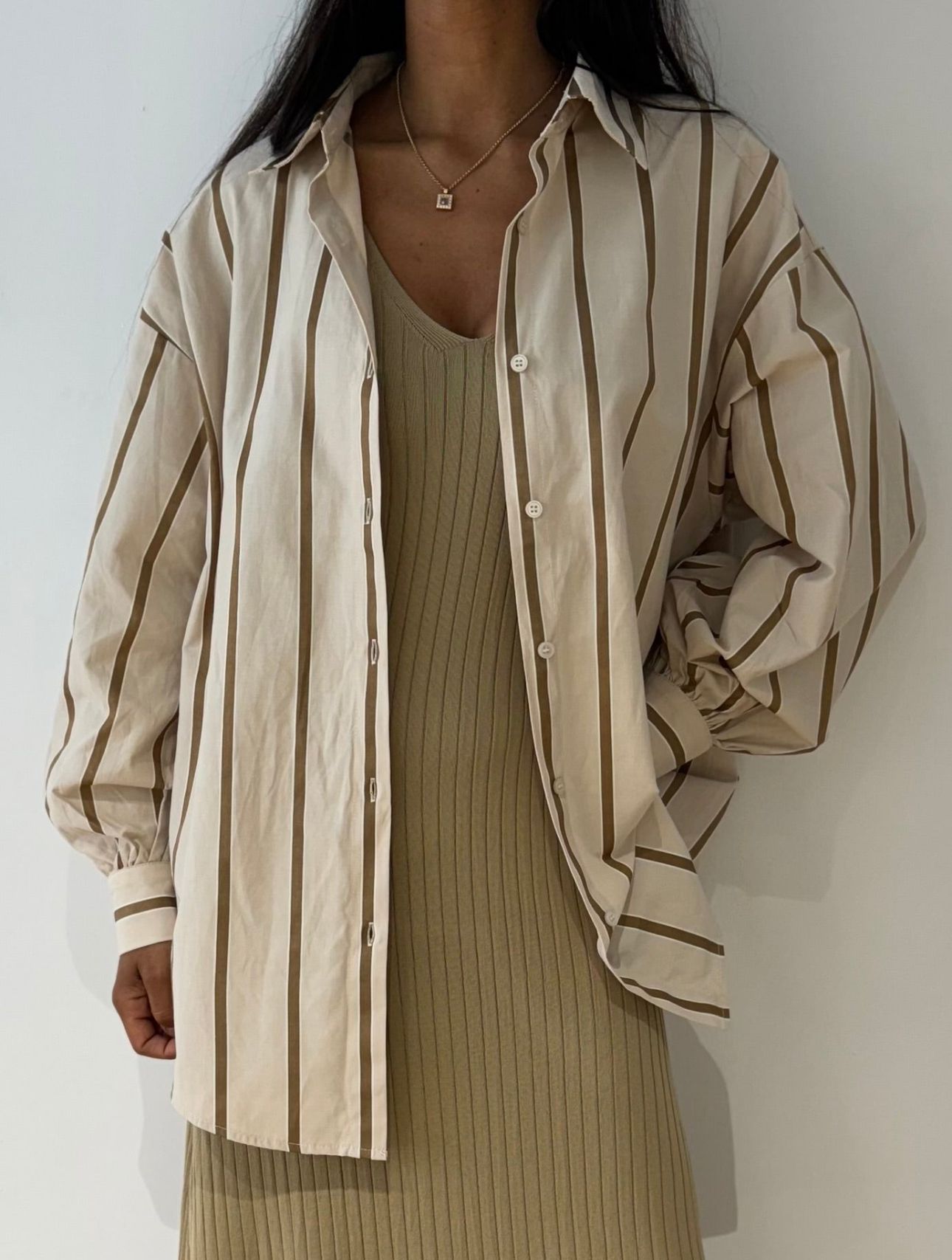 Femme portant une robe longue beige sans manche avec une chemise à rayures beige par-dessus.
