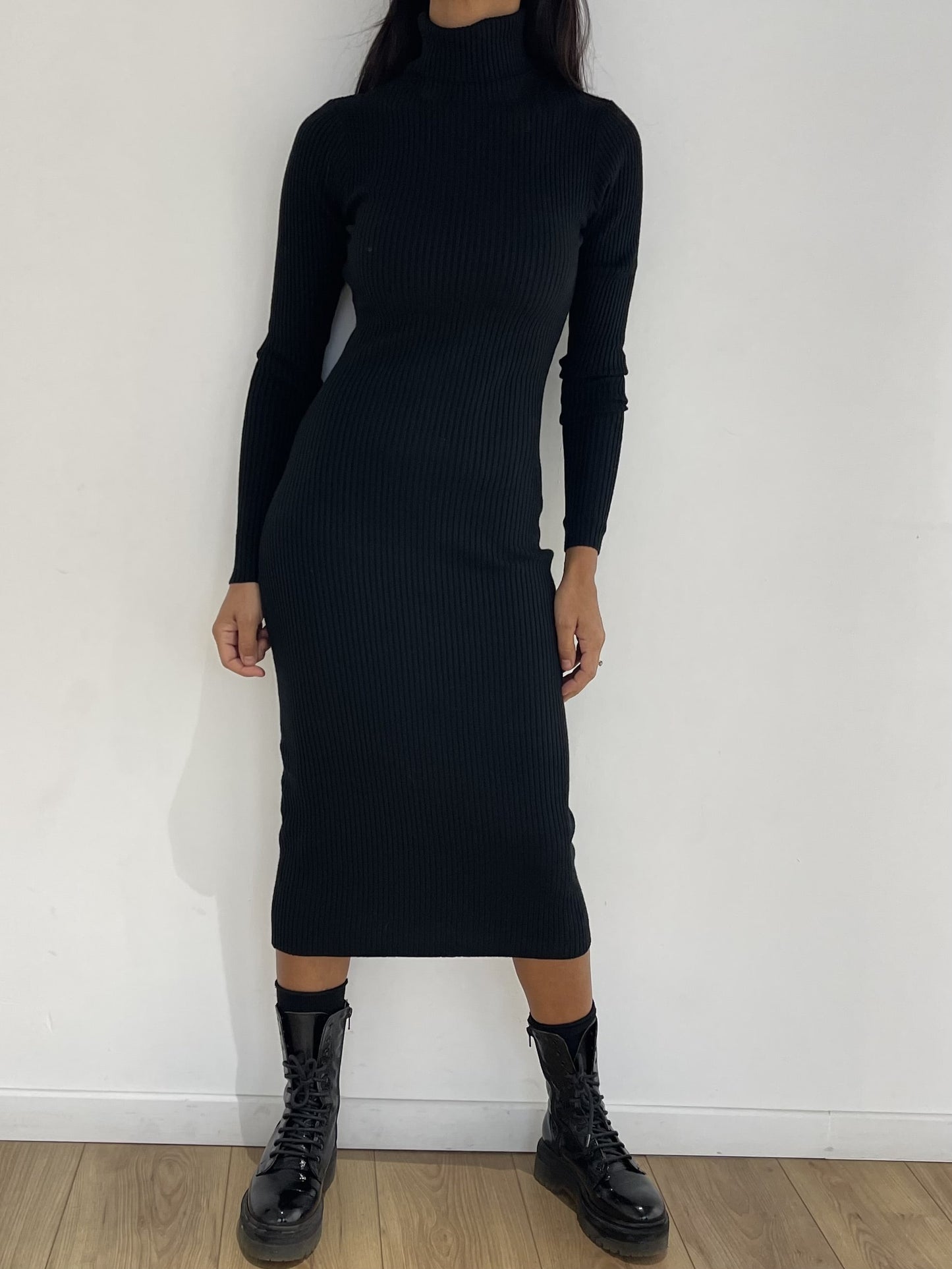 Robe mi-longue noire à col roulé, côtelée et élégante, assortie à des bottes noires pour un style cocktail chic.
