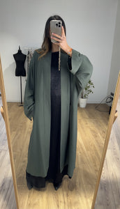 Femme combinant une robe noire et un manteau vert pour Ramadan