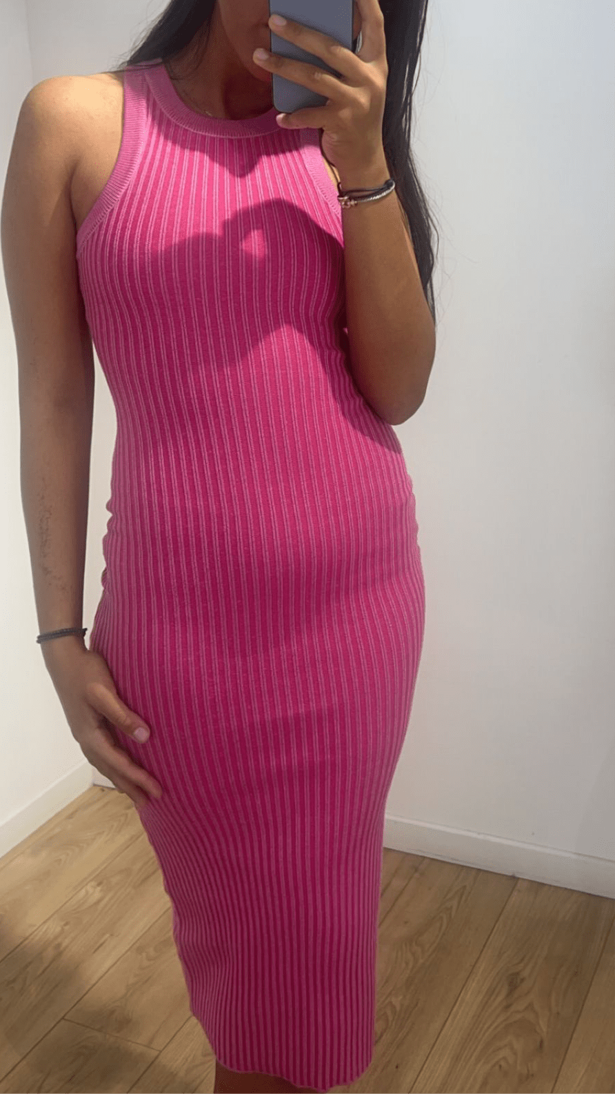 Femme portant une robe sans manches ajustée rose devant un miroir.