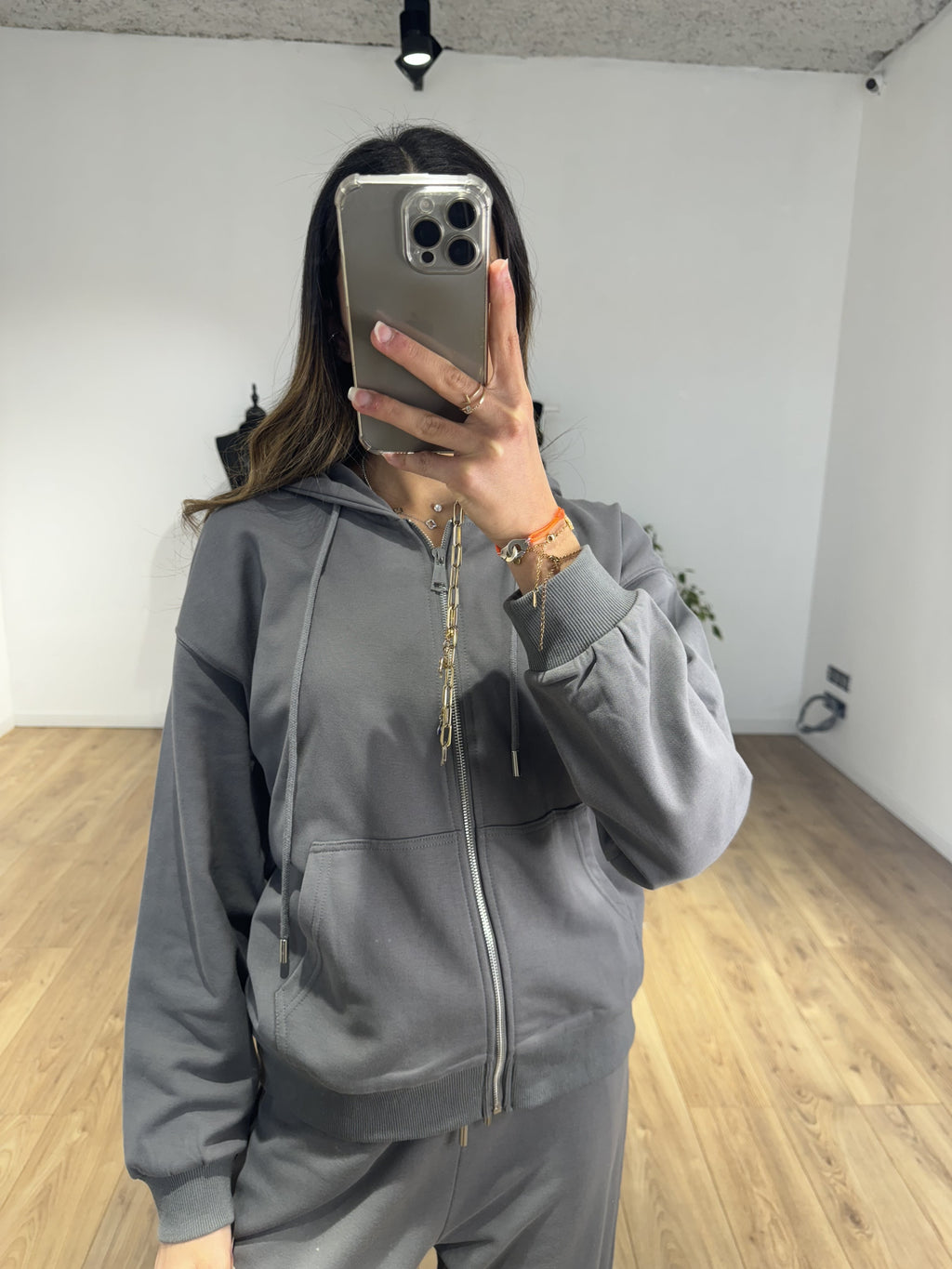 Femme portant un sweat à capuche zippé gris avec téléphone en main dans un intérieur moderne