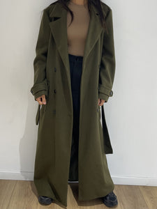 Femme portant un manteau long kaki ouvert dans un style urbain décontracté.