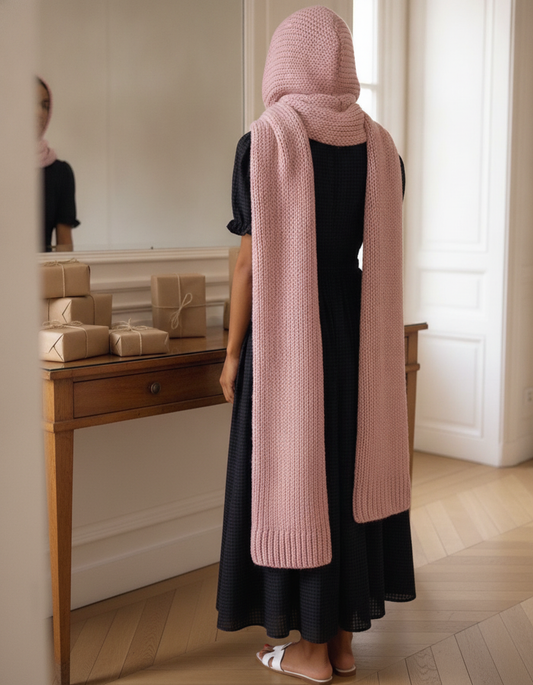 Idée cadeau Noël femme : écharpe à capuche en laine rose portée devant des cadeaux emballés