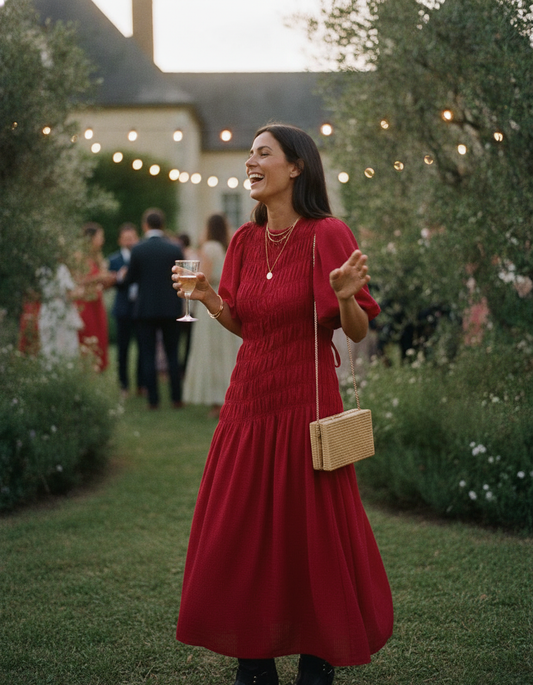 Invitée de mariage en robe smockée rouge Kata Paris dans un jardin de château au coucher du soleil