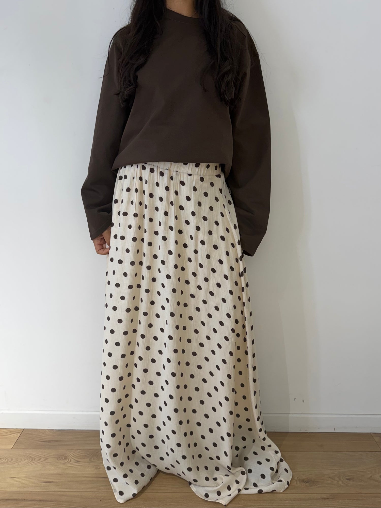 Vêtements capsule de printemps pour femme : jupe longue à pois, blazer sans manche et pantalons modernes sur fond neutre