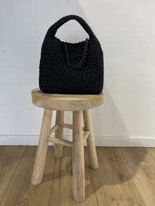 Petit sac à main Sacs Tega noir au design tressé sur un tabouret en bois, idéal pour une élégance quotidienne.
