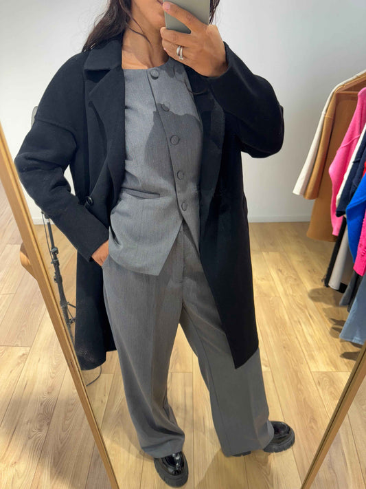 Femme portant un blazer sans manches gris avec un manteau noir, vue de face.