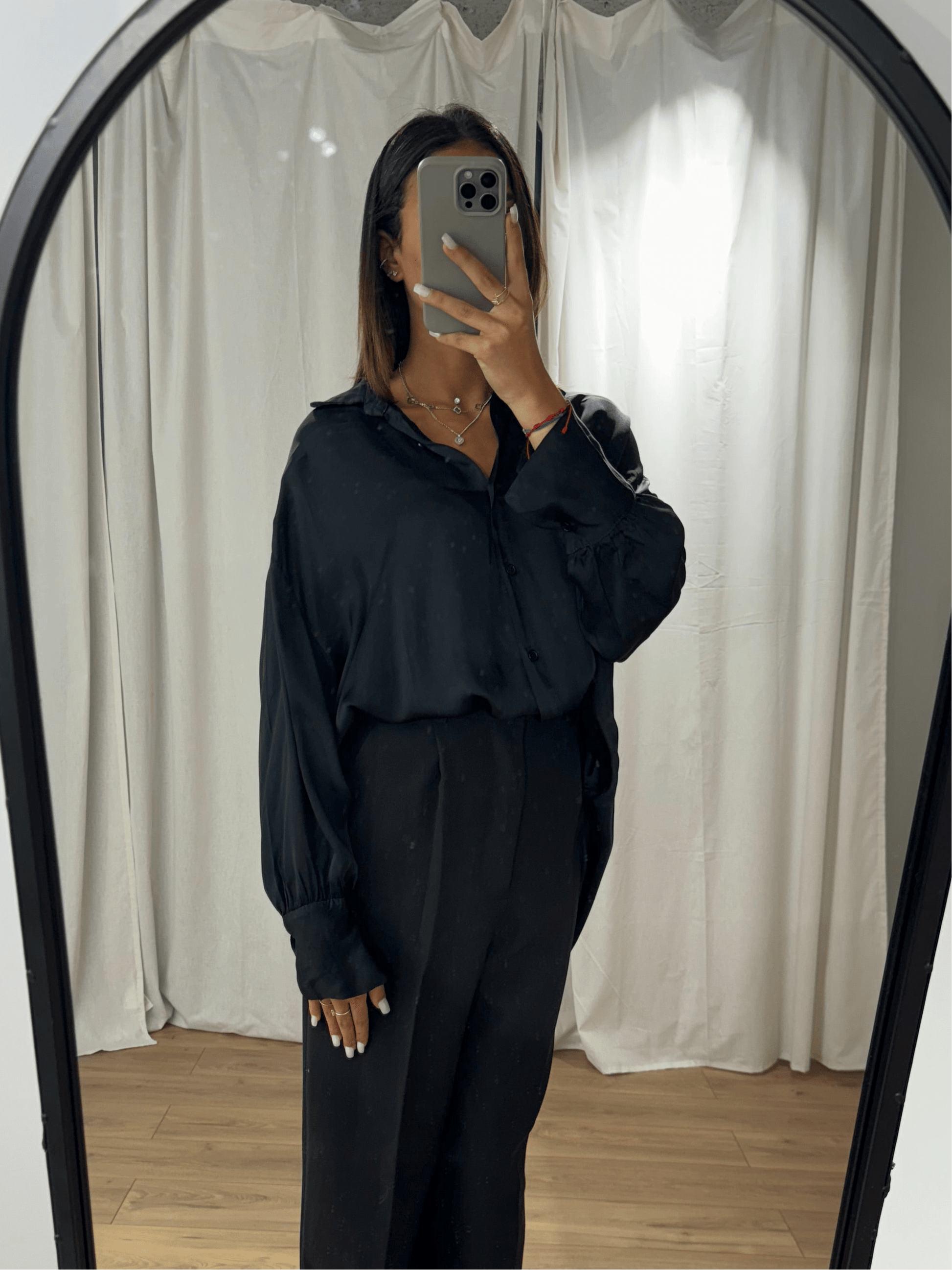 Femme portant une chemise en soie noire avec manches longues, vue de face dans un miroir.