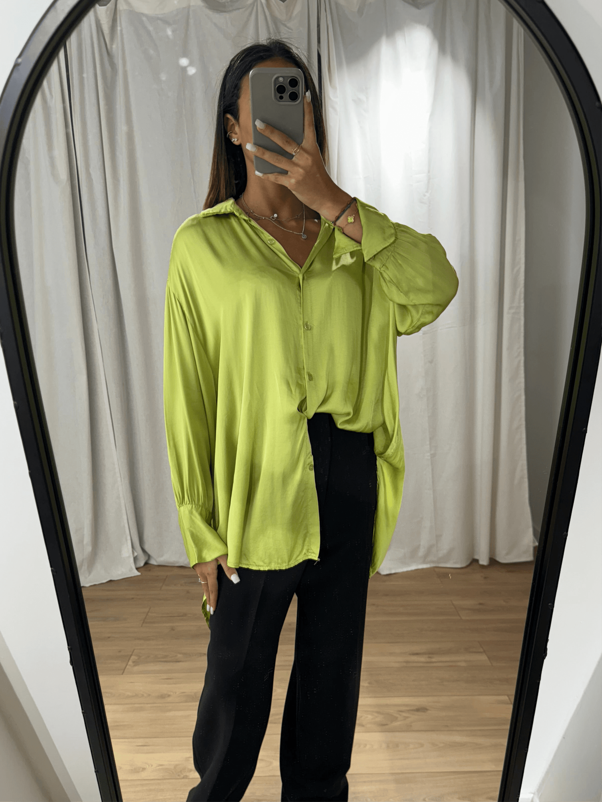 Femme portant une chemise en soie verte fluide avec manches longues, vue de face devant un miroir.