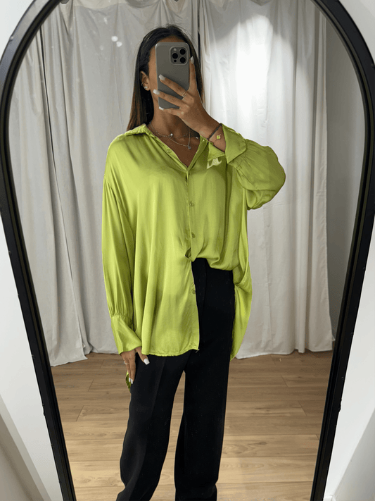 Femme portant une chemise en soie verte fluide avec manches longues, vue de face devant un miroir.