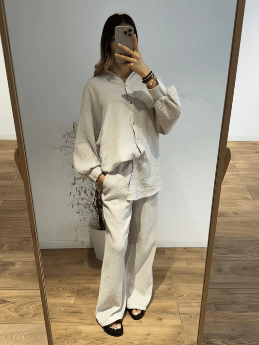 Femme portant un ensemble chemise et pantalon en gaze de coton beige, prise en selfie dans une pièce bien éclairée.
