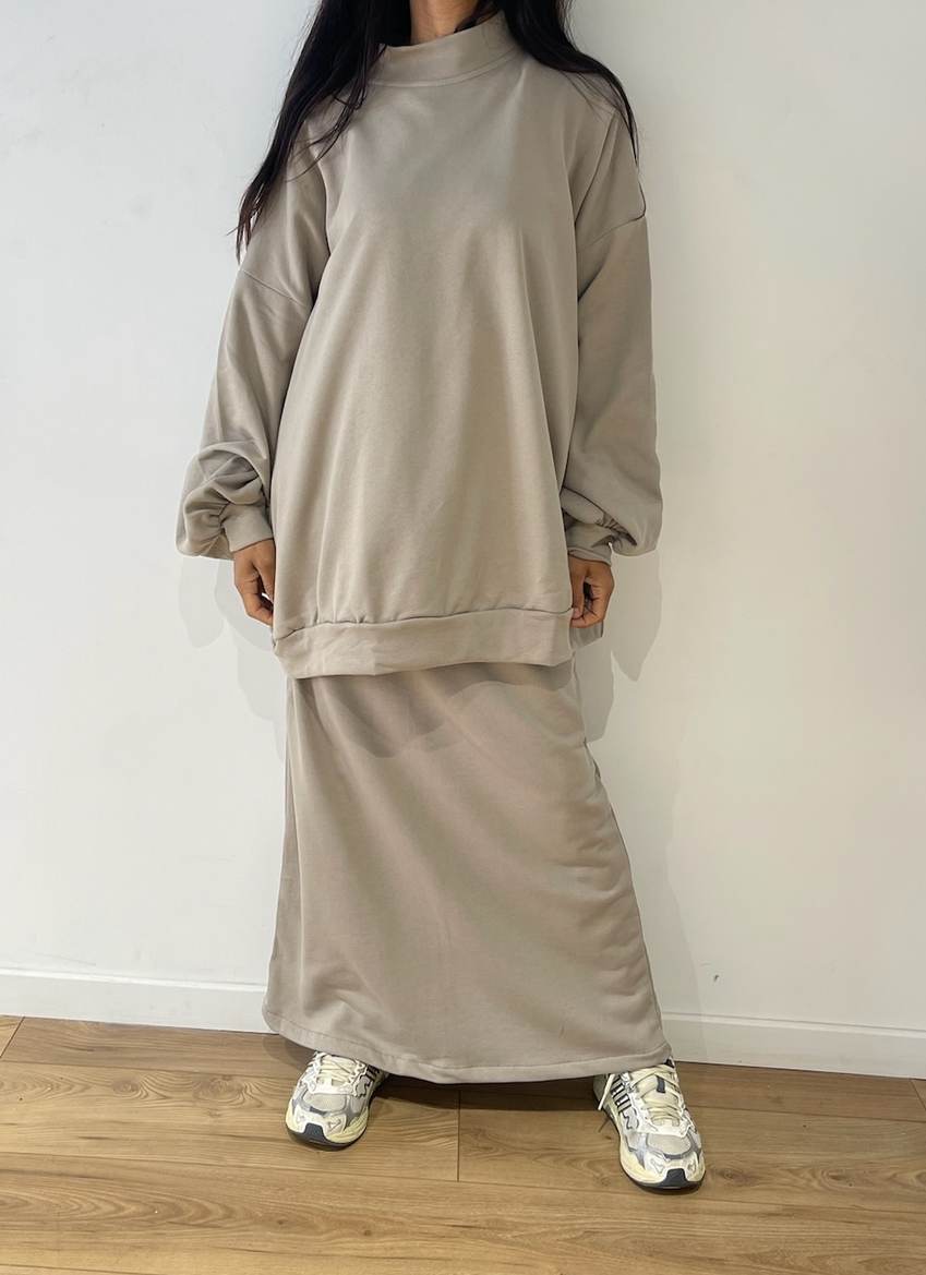 Femme debout en tenue décontractée beige, ensemble jupe et pull