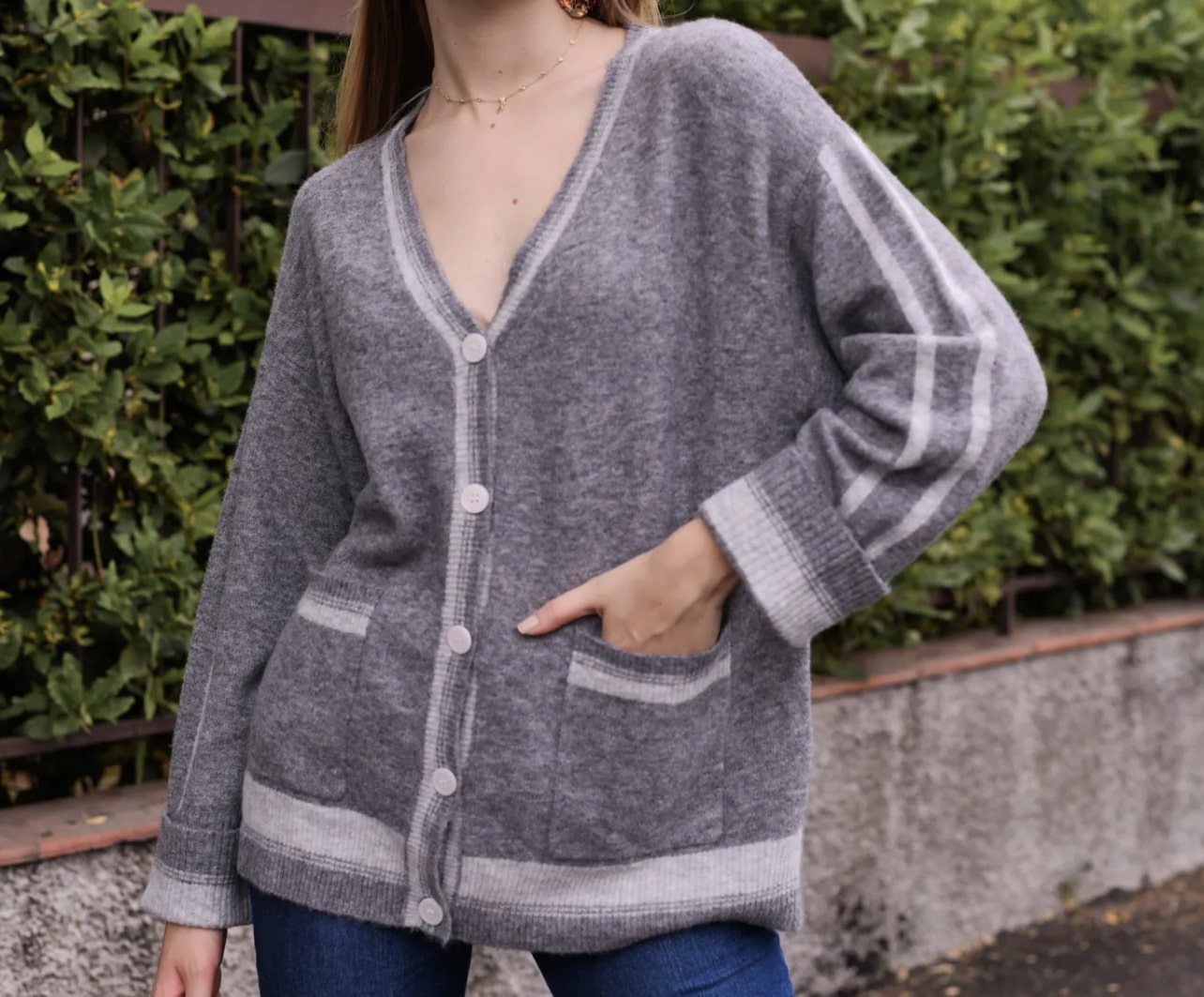 Gilet en laine gris clair avec détails de rayures blanches et poches, une addition versatile à toute tenue automnale.