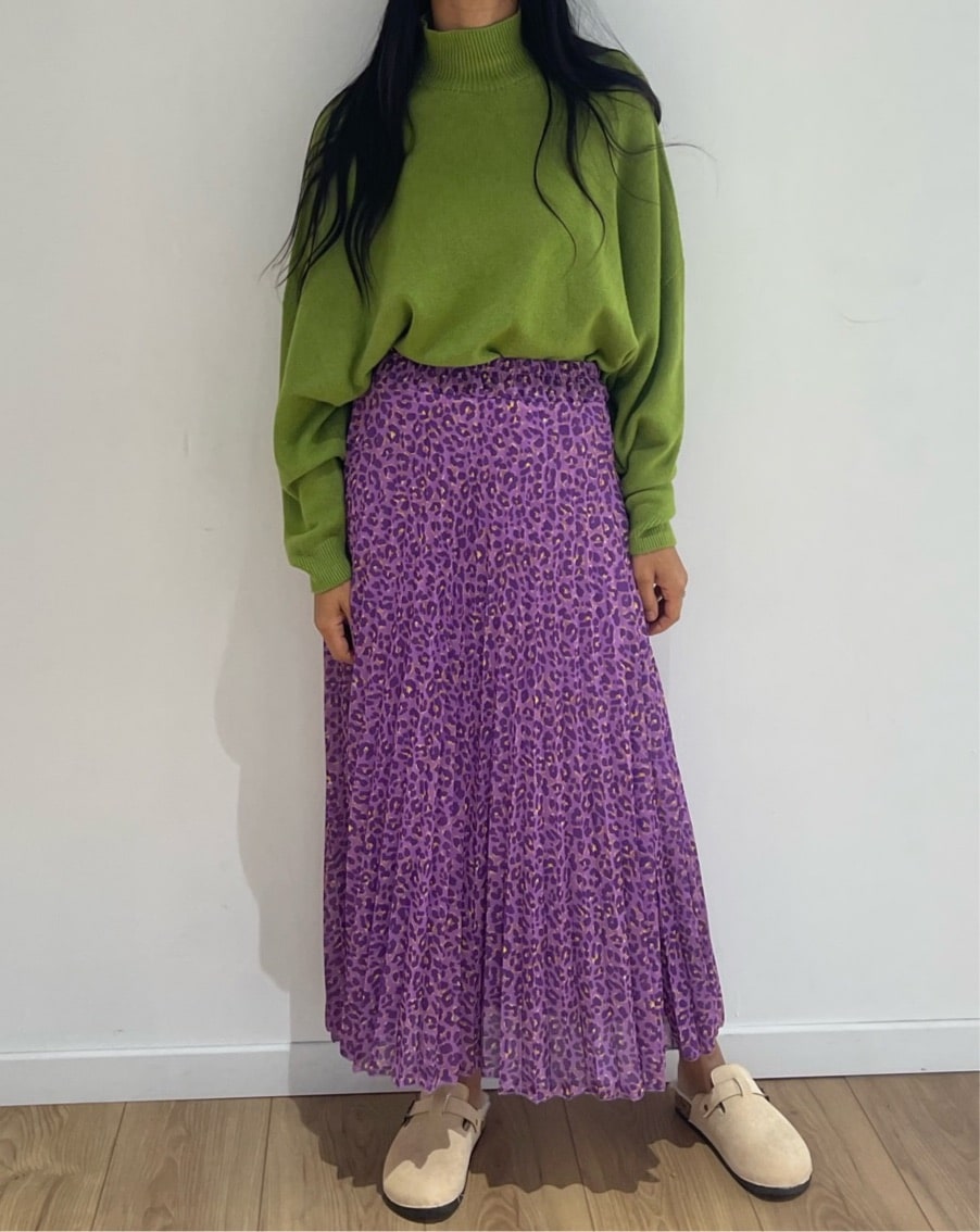 Jupe longue plissée à imprimé léopard vert associée à un pull violet vif pour un style remarquable.