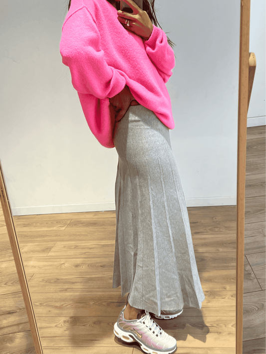 Femme portant une jupe longue grise plissée avec un pull rose vif, vue de profil.