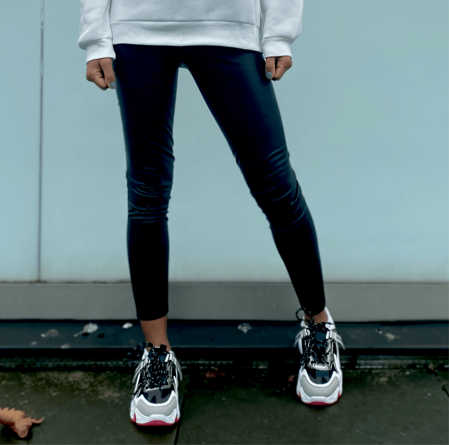 femme portant des leggings noirs en simili cuir avec un sweat à capuche blanc pour un look urbain