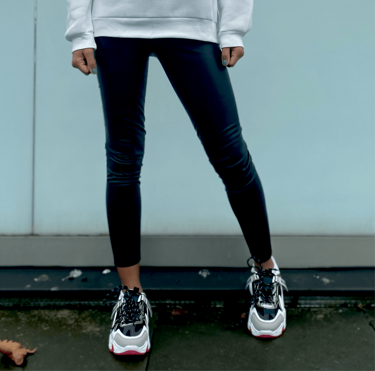 femme portant des leggings noirs en simili cuir avec un sweat à capuche blanc pour un look urbain