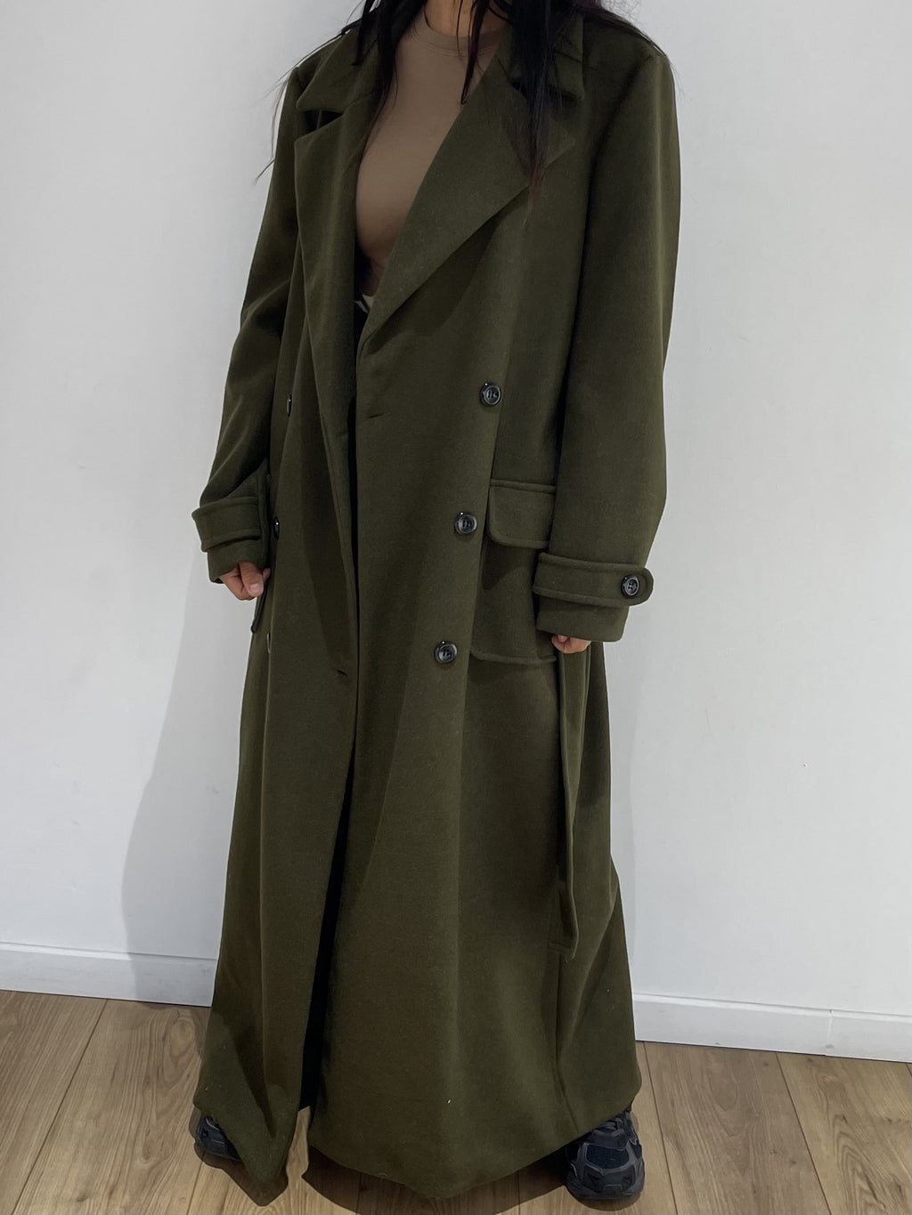 Manteau long kaki pour femme boutonné, démontrant la coupe et le design.