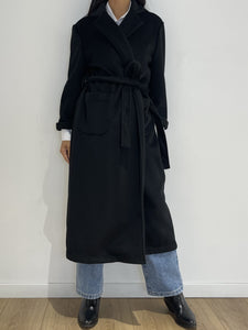 Manteau noir long à ceinture de chez Kata Paris, porté par une femme pour une silhouette raffinée et contemporaine.