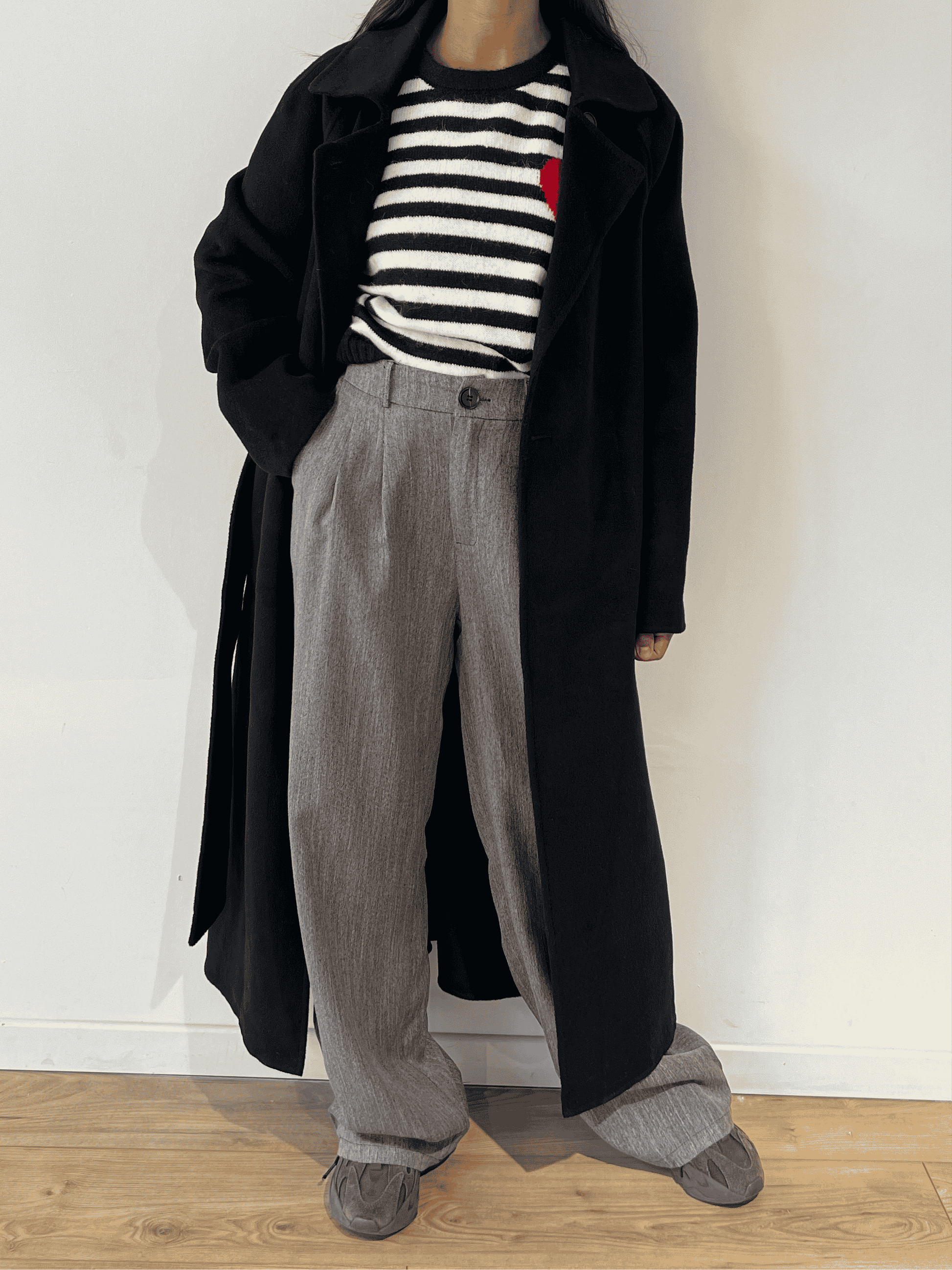 Long manteau noir porté sur un pull marinière et un pantalon gris.