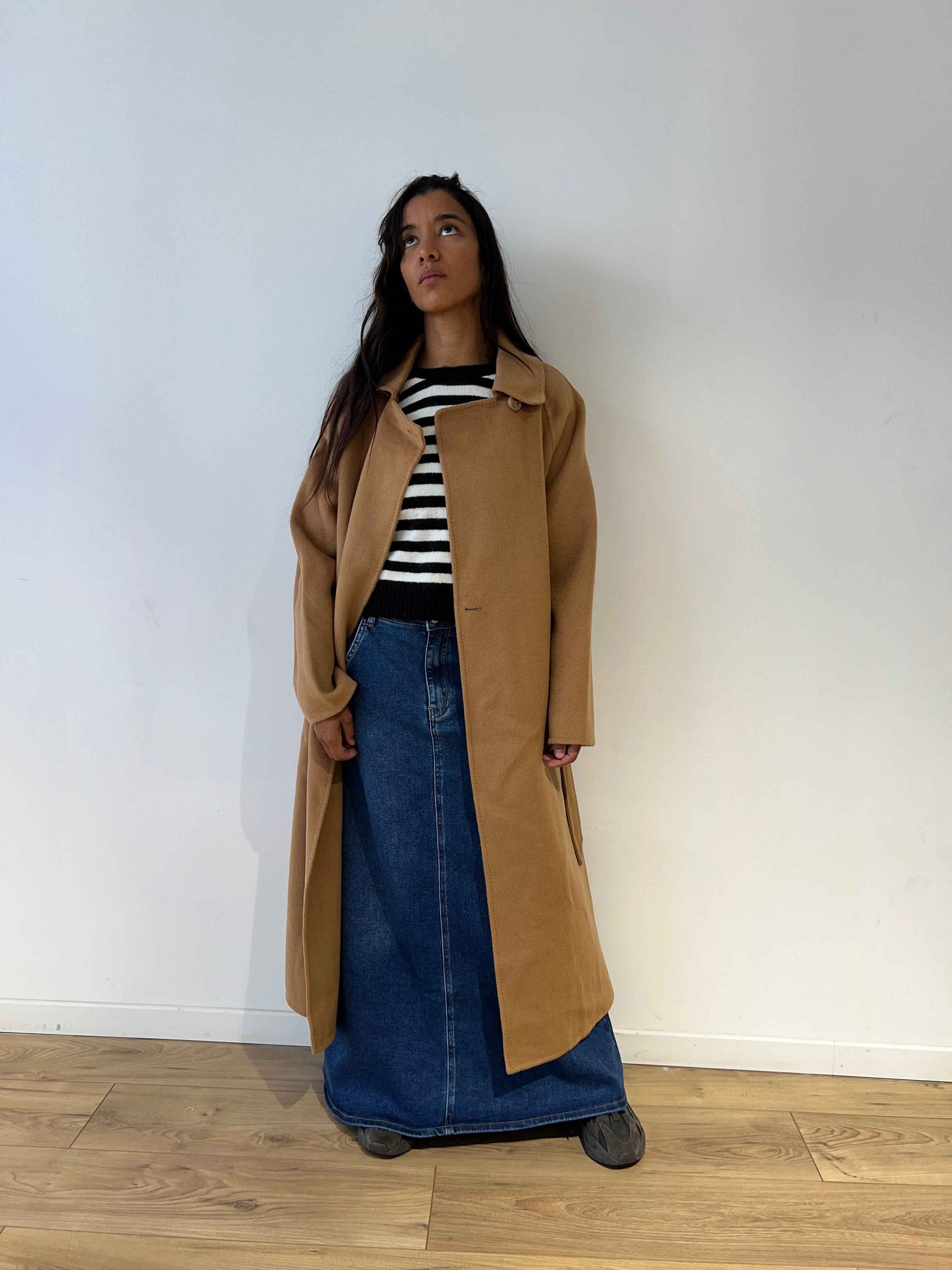 Femme portant un pull marinière noir et blanc avec un cœur rouge, look complet avec manteau camel et jupe en denim, vue de face.