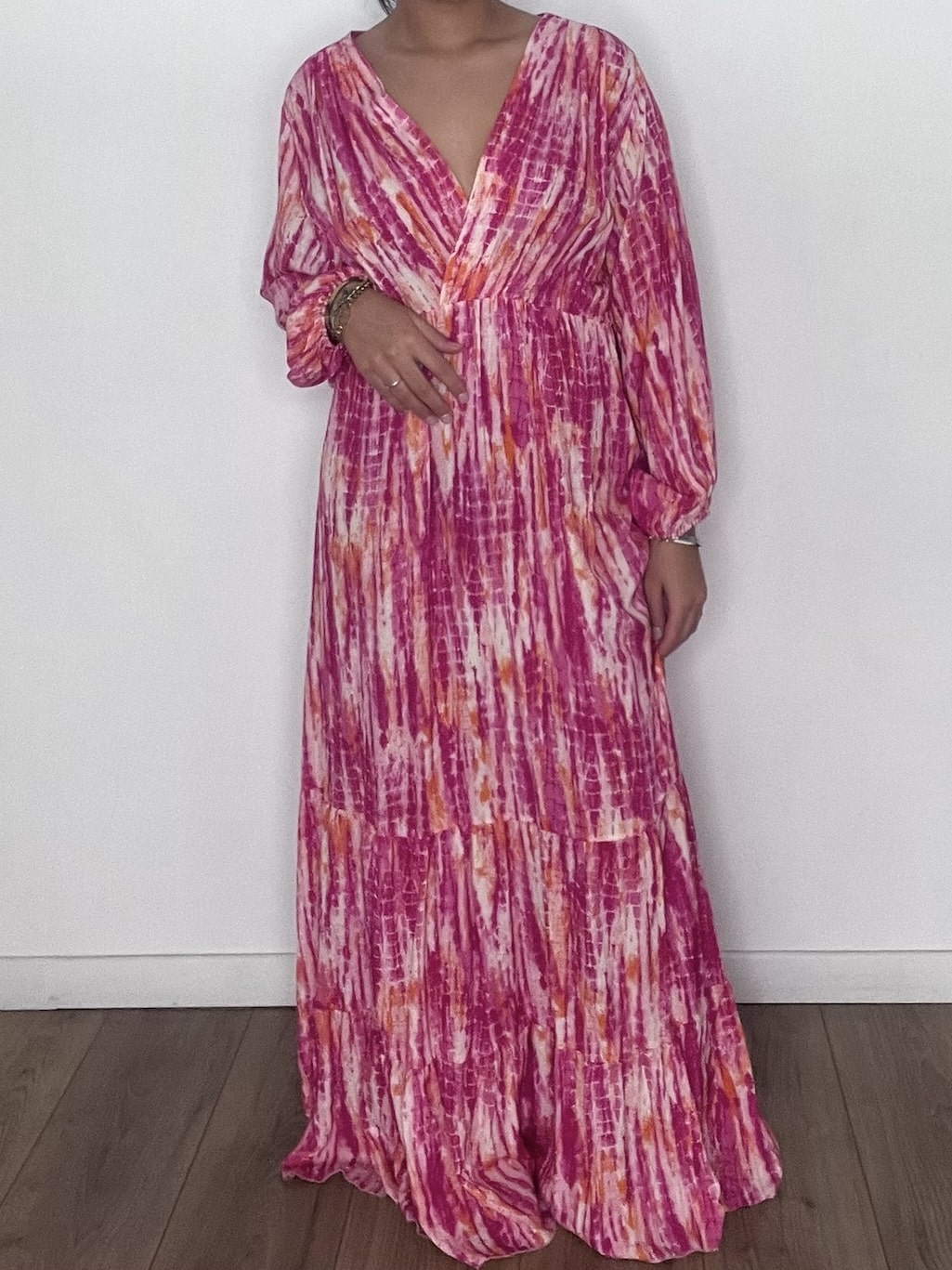 Femme portant une robe longue tie and dye en soie rose, prise en selfie devant un mur blanc.