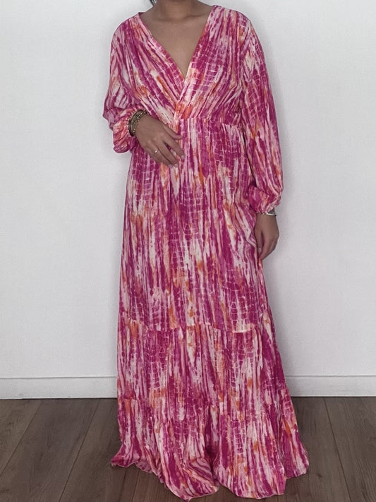Femme portant une robe longue tie and dye en soie rose, prise en selfie devant un mur blanc.