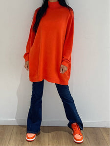 Robe-pull orange vif associée à un jean pour un style décontracté et audacieux.