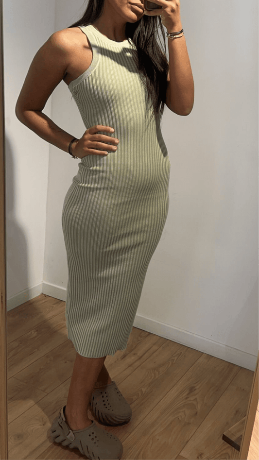 Femme portant une robe sans manches ajustée verte devant un miroir.