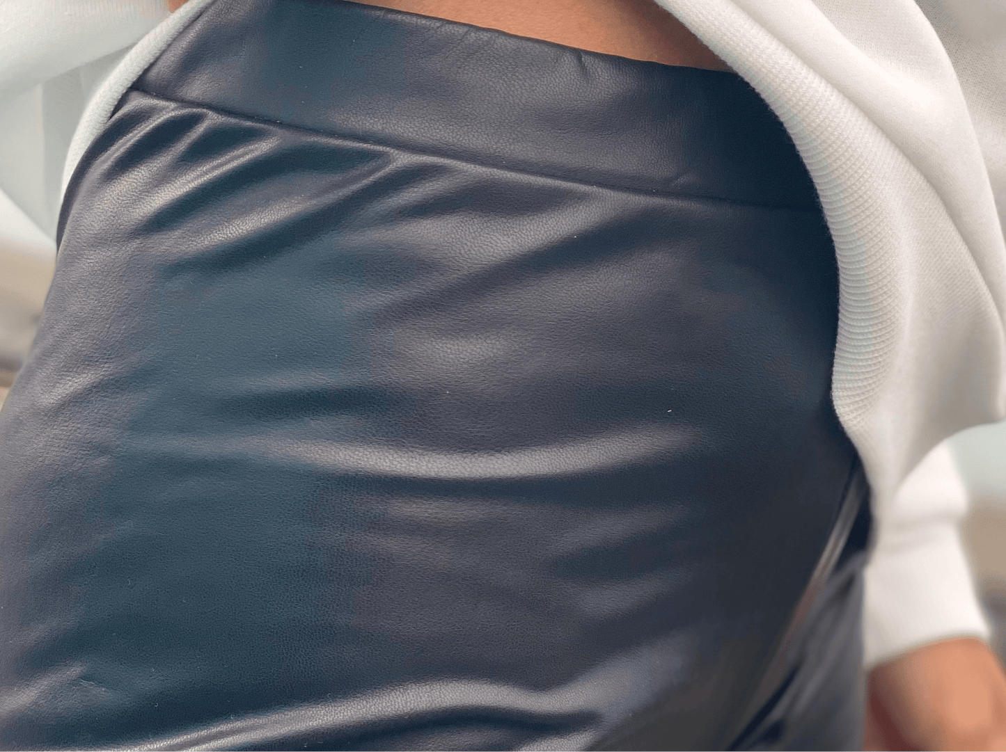 détail de texture de legging en simili cuir noir porté sous un sweat blanc